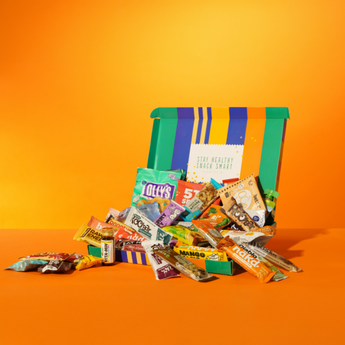 Zakelijke box met gezonde tussendoortjes zoals snacks en energierepen op een kleurrijke achtergrond.